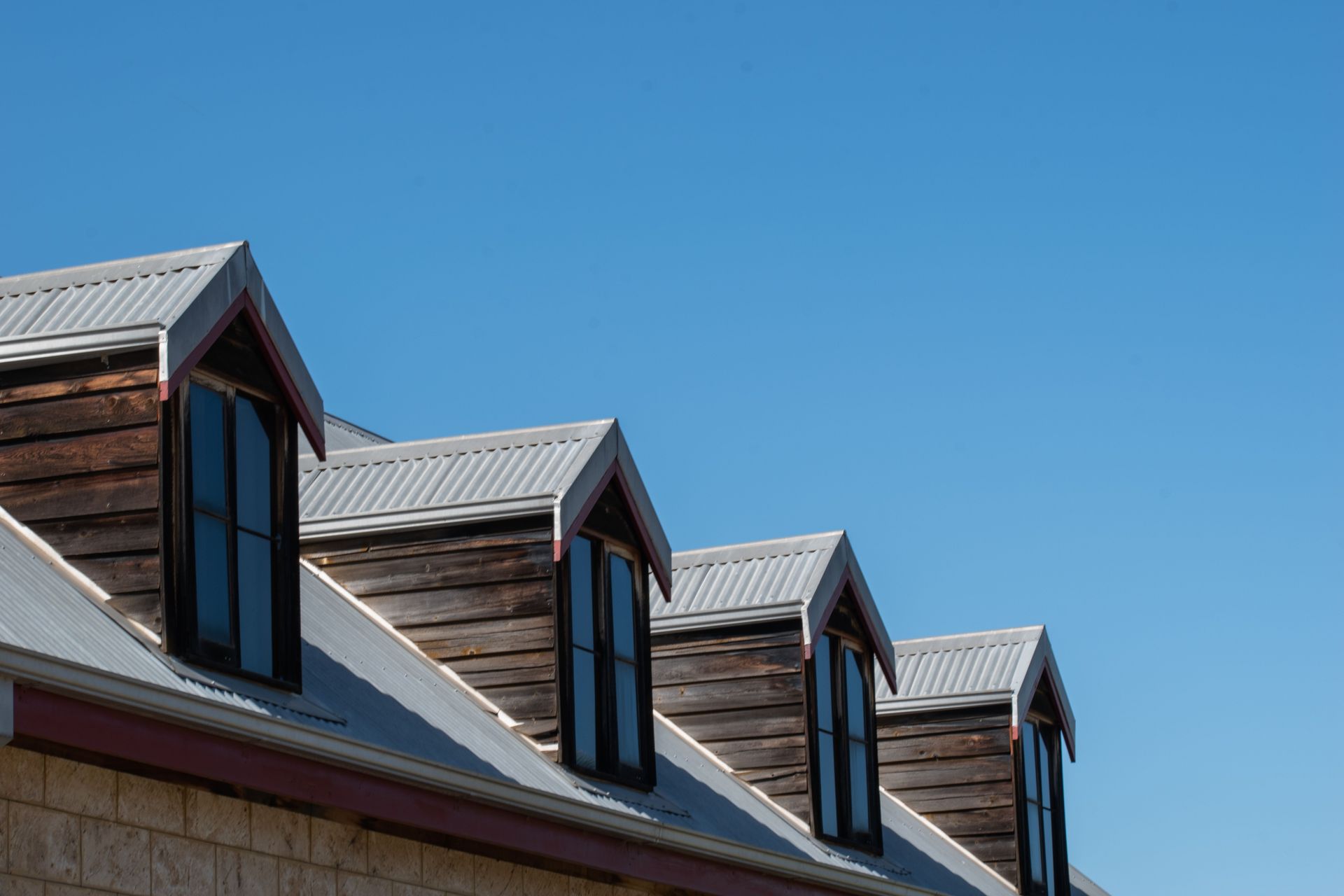 Modern triangular rooftops with windows against a clear blue sky.