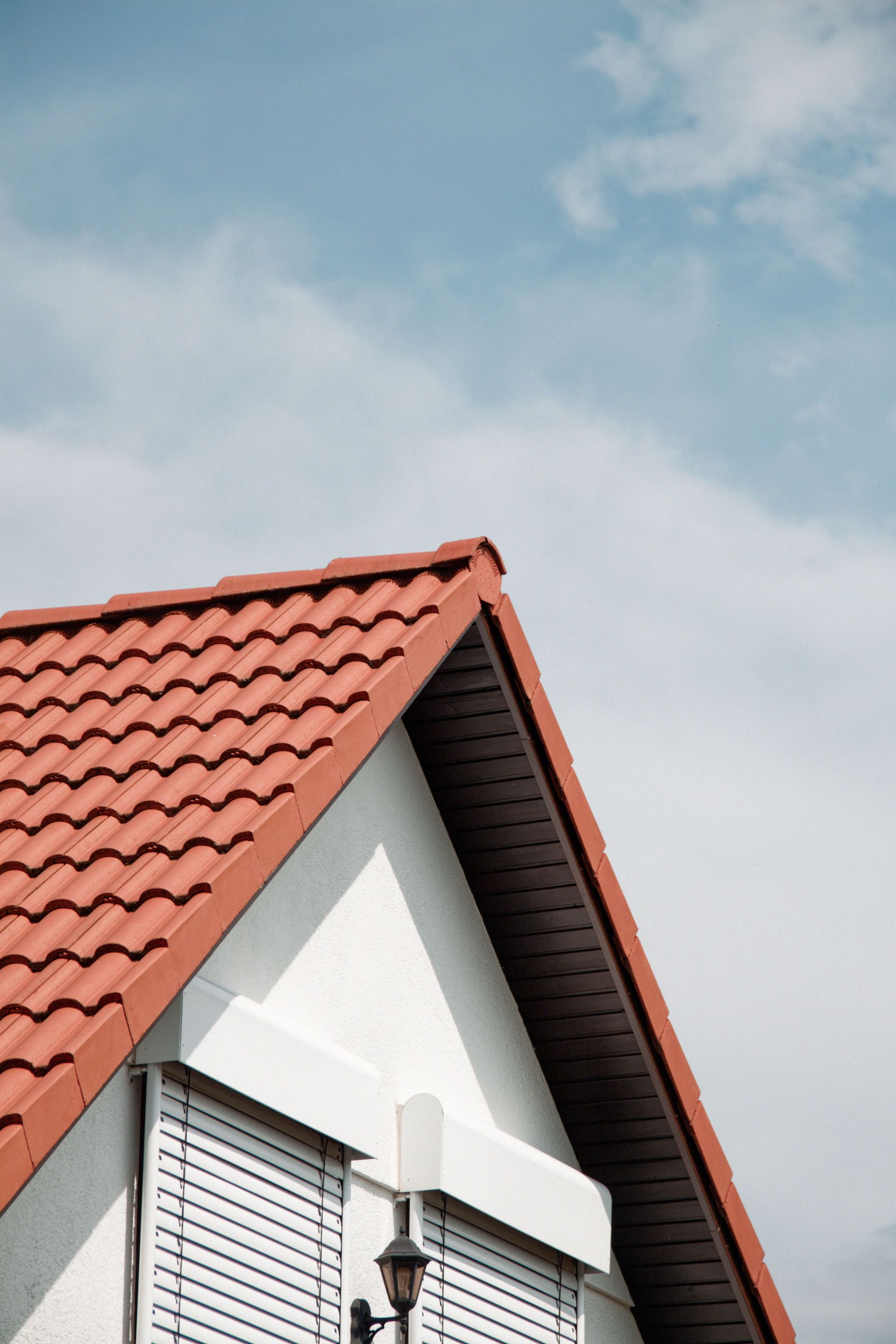 Close-up of a modern house's red tile roof and shutters against a bright sky, showcasing architectural design.
